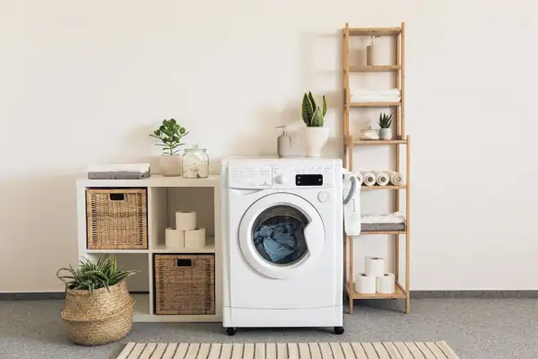 Waschmaschine mit Aquastop, die undicht ist, steht neben einem Regal mit Handtüchern und Pflanzen.