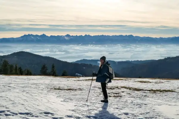 Kobieta z kijkami trekkingowymi na ośnieżonym szczycie, podziwiająca Tatry. To najładniejsza trasa na Turbacz zimą.