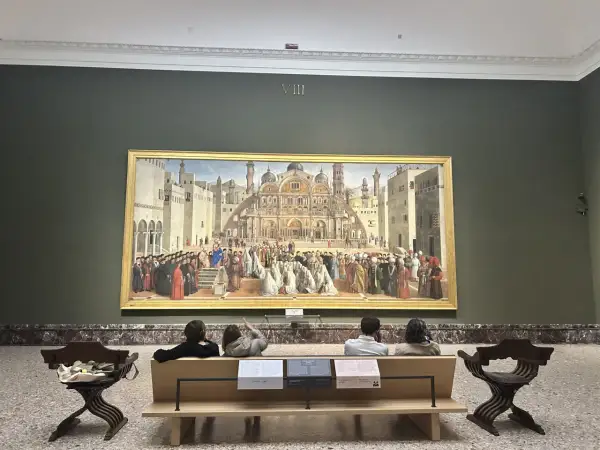 A grand painting depicting a historical scene is the centerpiece of this art in Milan gallery. Visitors sit on a bench, contemplating the detailed artwork.
