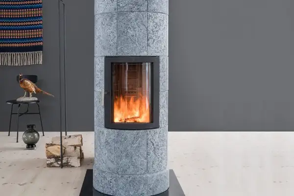 Poêle en pierre ollaire aux flammes vives, avec une décoration de faisan et de bois de chauffage à proximité.