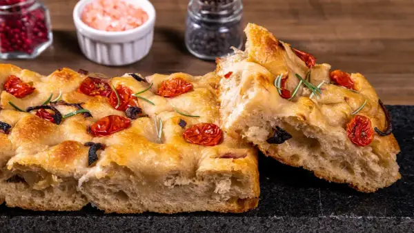 Złocista focaccia z pomidorkami koktajlowymi i rozmarynem, z widocznym puszystym wnętrzem.