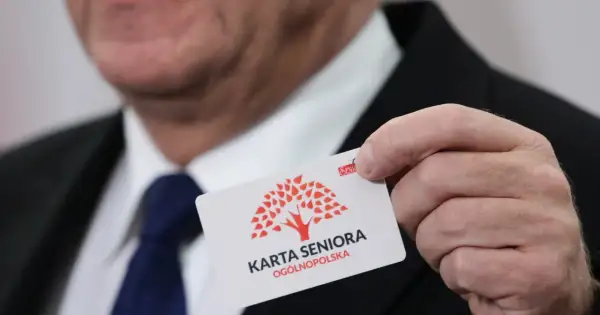 Mężczyzna prezentuje kartę seniora z czerwonym drzewem. To ogólnopolska karta uprawniająca do zniżek.