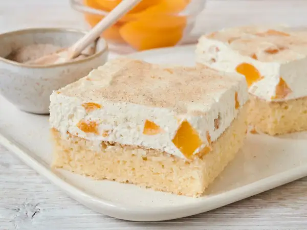 Saftiger Pfirsich Schmand Kuchen mit zarter Sahne und Zimt bestreut. Ein Genuss für jeden Anlass.