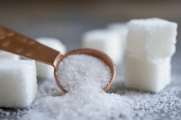 Łyżeczka z kryształkami, obok kostki cukru. Czy to sorbitol? Ten słodzik jest często używany jako zamiennik cukru.