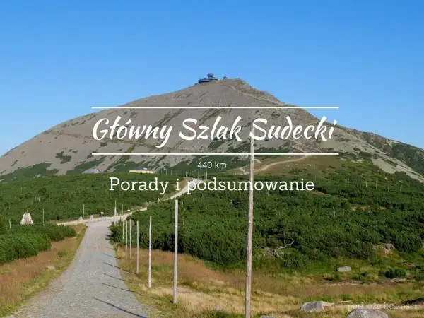 Główny Szlak Sudecki, 440 km. Widok na górę ze szczytem i budynkami, droga kamienista, zieleń.