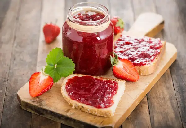 Confiture de fraises sur pain grillé, un délice qui peut faire grimper le cholestérol. Fraises fraîches et une feuille verte sur fond de bois.