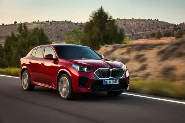 Czerwone BMW X2 2025 pędzi po pustynnej drodze, otoczone suchymi wzgórzami i drzewami.