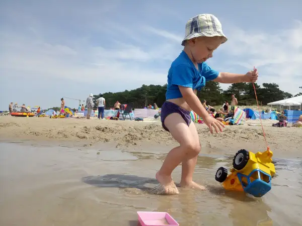 Chłopiec ciągnie zabawkowe auto po plaży w Darłowie. To świetne darłowo atrakcje dla dzieci, gdzie można się bawić w wodzie i piasku.