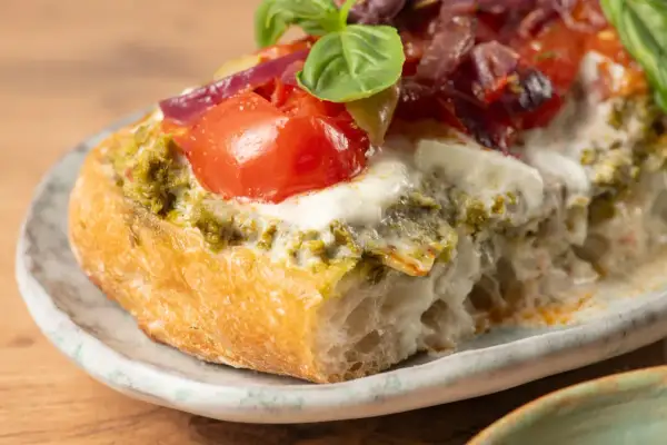 Bruschetta au pesto, tomates fraîches, mozzarella fondante et oignons rouges sur une tranche de pain grillé. Un délice !