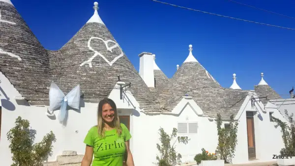 Una donna sorride davanti ai trulli di Alberobello, patrimonio UNESCO, con un grande fiocco azzurro appeso a un cono.