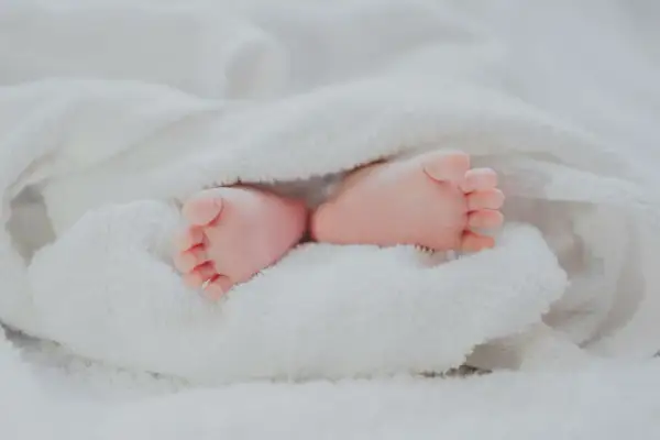 Petits pieds roses d'un bébé, emmitouflés dans une couverture blanche. Quel jour pour un baptême, une nouvelle vie commence !
