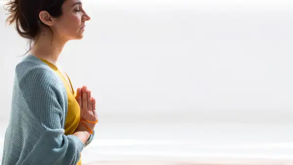 Mujer meditando con las manos juntas en posición de oración, reflejando el namasté significado yoga.