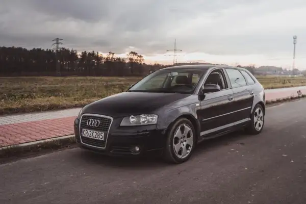 Czarne Audi A3 2009 na tle zachodzącego słońca i linii energetycznych.