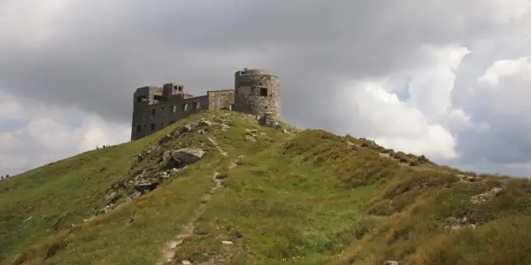 Kamienny zamek na szczycie zielonych gór w Ukrainie, pod burzliwym niebem.