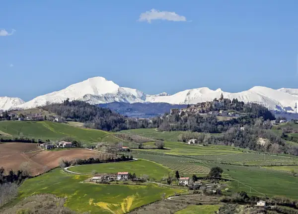 Paesaggio collinare con un borgo in cima, montagne innevate sullo sfondo. Un tranquillo scorcio del fermo provincia.