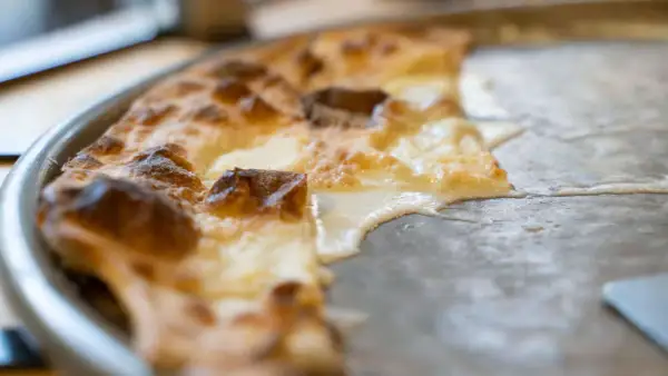 En bit av en gyllene focaccia di Recco med smält ost som rinner ut på en plåt.