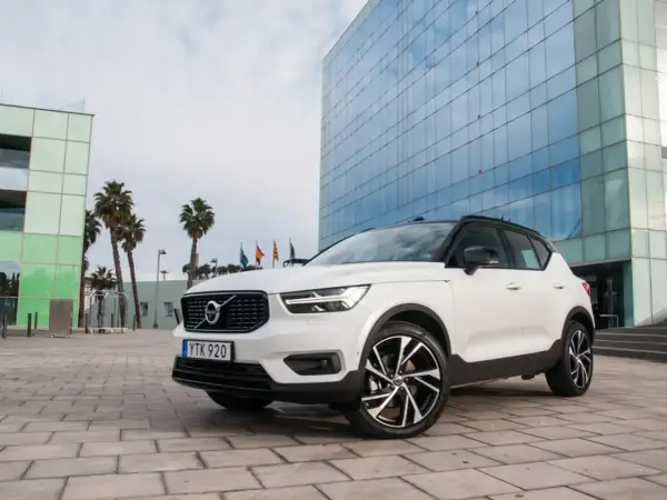 Białe Volvo XC40 z czarnym dachem zaparkowane przed nowoczesnym budynkiem z niebieskimi oknami.
