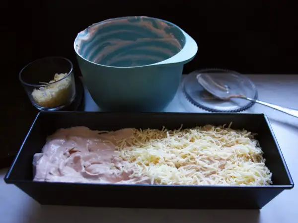 Förberedelser för ett gott kassler recept: en form med kassler och ost, en skål med riven ost och en tom blandskål.