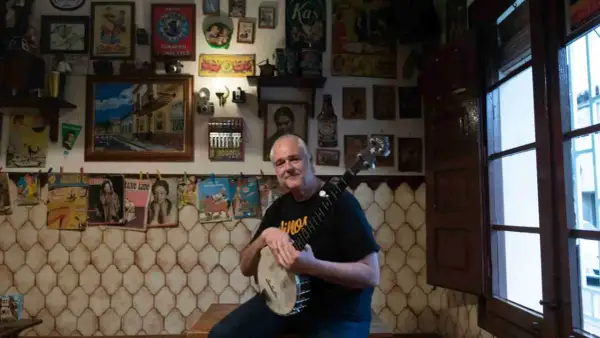Un hombre sonriente con un banjo en salsipuedes una tasca encantadora, rodeado de carteles vintage y objetos curiosos.