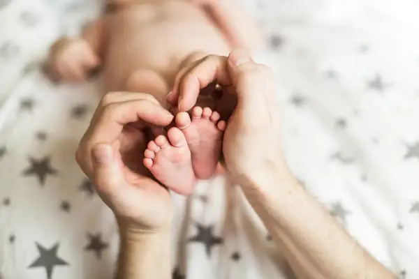 Dłonie otaczają maleńkie stópki 7 tygodniowego dziecka. Delikatne paluszki i pięty są objęte czułością.