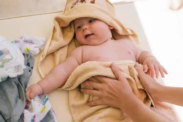 Söt bebis i handduk, kanske med tyst reflux bebis symtom. Bredvid ligger kläder och blöjor.