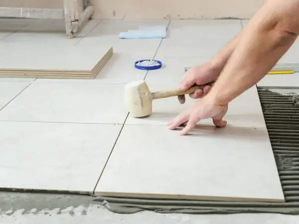 Pose de carrelage sans plinthe, un artisan ajuste une dalle avec un maillet en caoutchouc sur le mortier frais.