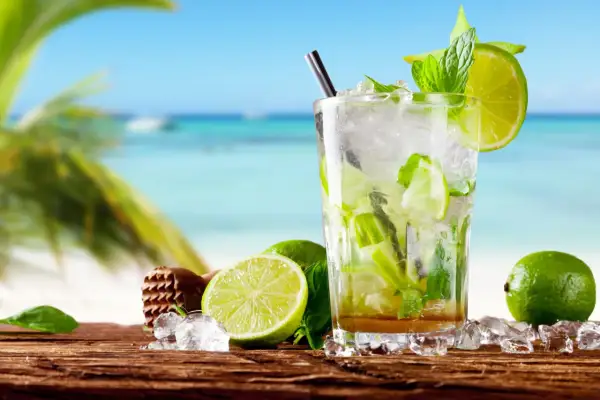 Orzeźwiający mohito czy mojito na plaży? Szklanka pełna lodu, mięty i limonki, z widokiem na turkusowe morze i palmę.