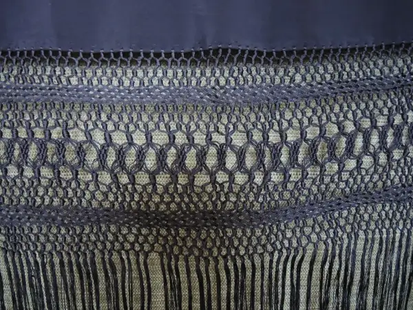 Detalle de cómo hacer flecos para mantones, con un intrincado tejido de macramé y borlas.
