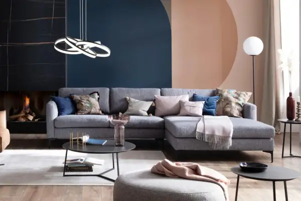 Ein hellgraues Sofa dekorieren mit Kissen in Rosa, Blau und floralen Mustern. Eine Decke liegt darüber.