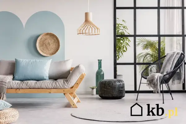 Sofa z poduszkami w kolorze baby blue, czarne krzesło z kocem, zielona butelka i rośliny w nowoczesnym wnętrzu.