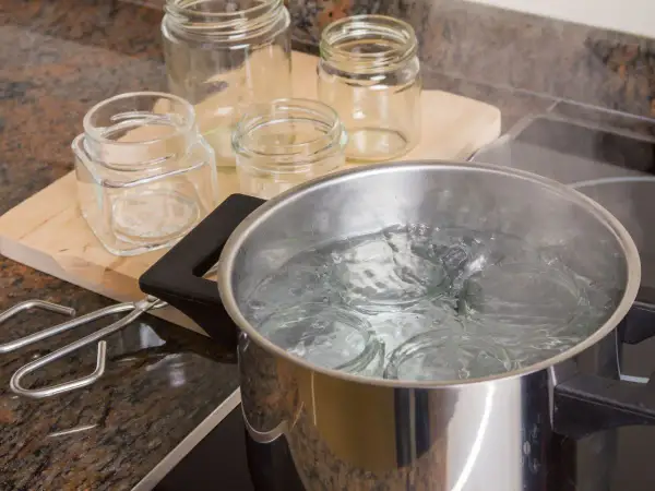 Gläser werden für das Einkochen mit Schraubdeckel sterilisiert. Ein Topf mit kochendem Wasser und ein Glasheber liegen bereit.