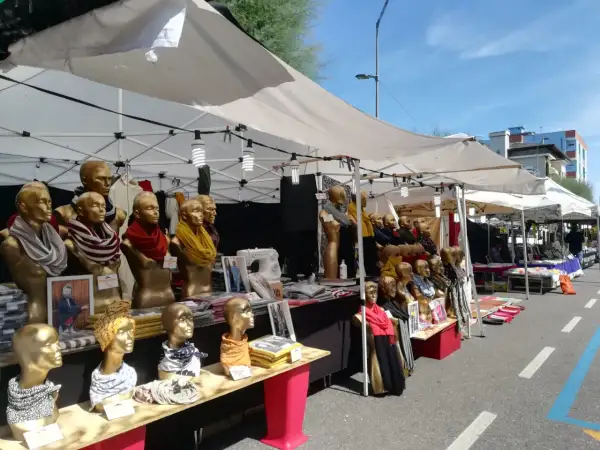 Bancarelle colorate alla fiera di Fano, con manichini dorati che indossano sciarpe e foulard.