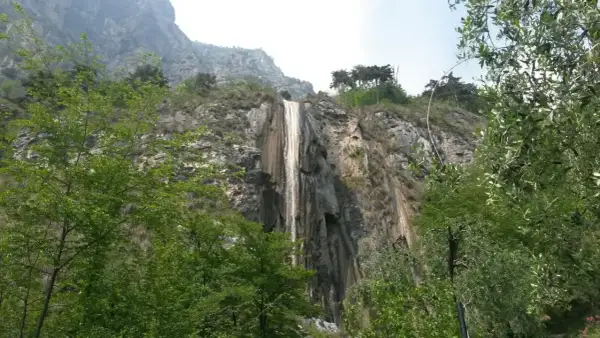 Cascata del Sopino, un velo d'acqua scende da una parete rocciosa circondata da vegetazione lussureggiante.
