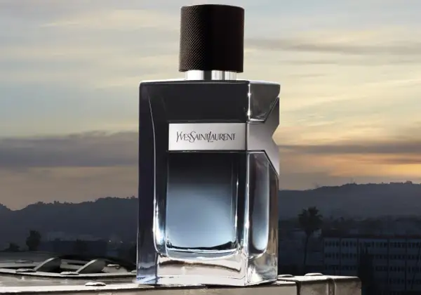Elegancka butelka YSL EDP na tle zachodzącego słońca nad miastem.