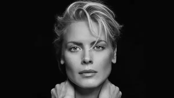 Synnøve Macody Lund, mit ihrem markanten Blick und den Händen am Hals, posiert in einem dramatischen Schwarz-Weiß-Porträt.