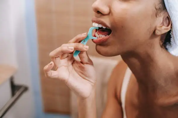 Mujer usa hilo dental, evitando errores al cepillarse los dientes.