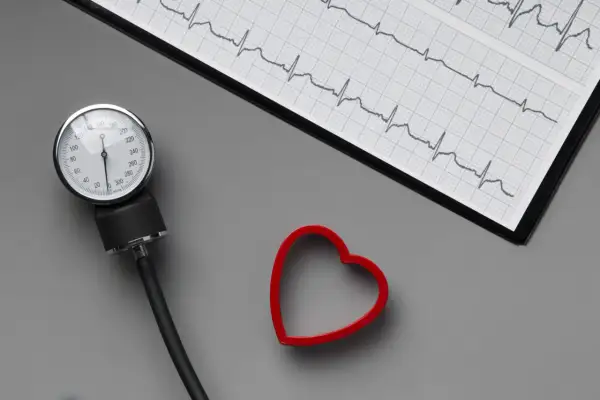 Ciśnieniomierz, EKG i czerwone serce na szarym tle.