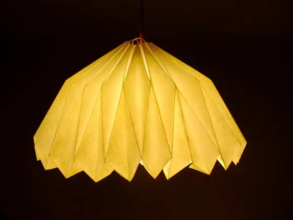 Oświetlony, żółty abażur z papieru, złożony jak origami. Inspiracja, jak zrobić abażur z papieru, dla Twojego wnętrza.