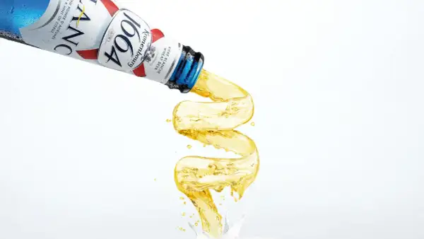 Piwo w niebieskiej butelce Kronenbourg 1664 leje się w fantazyjny sposób, tworząc złoty strumień.