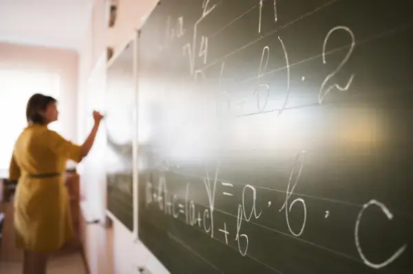 Nauczyciel dyplomowany pisze wzory matematyczne na tablicy.