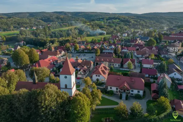 Widok z lotu ptaka na Lipnicę Murowaną. Widać kościół z wieżą, domy z czerwonymi dachami i otaczające lasy. To piękne miejsce oferuje wiele atrakcji.