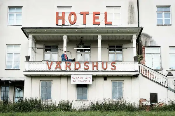 Man sitter på balkongen till ett gammalt värdshus med skylten "HOTEL VÄRDSHUS".