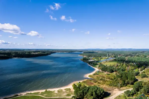 Malownicze jezioro Chańcza otoczone lasami, z piaszczystą plażą i zabudowaniami w tle.