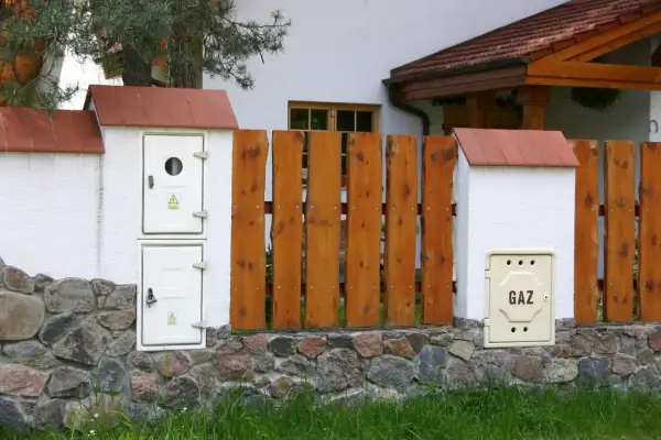 Zastanawiasz się, ile kosztuje ponowne podłączenie gazu do mieszkania w bloku? Na zdjęciu widzimy skrzynkę gazową z napisem "GAZ" przy kamiennym murku i drewnianym płocie.