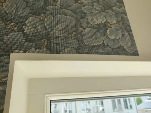 Detaljbild av en vägg med blått blommönster, visar hur tapetserar man runt ett fönster.