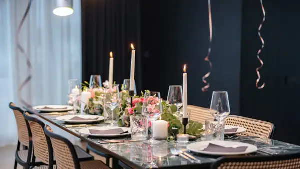 Tavola apparecchiata con candele, fiori rosa e bicchieri per un elegante servizio alla francese.