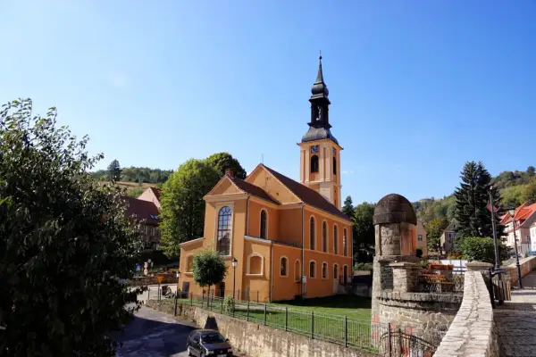 Pomarańczowy kościół z wieżą zegarową na rynku. W tle zielone wzgórza, przypominające srebrną górę.