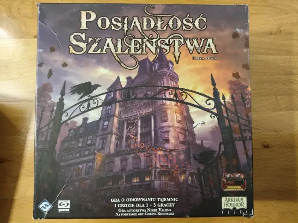 Okładka gry planszowej "Posiadłość Szaleństwa" z mroczną posiadłością i wronami. Scenariusze tej gry przeniosą Cię w świat tajemnic i grozy.