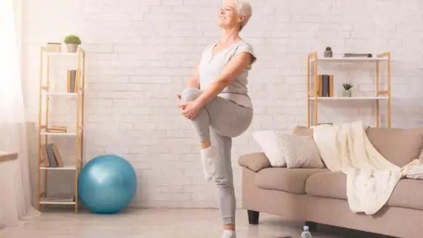 Une femme âgée sourit en faisant un exercice d'équilibre, idéal pour une fiche technique gym douce pour personne âgée.