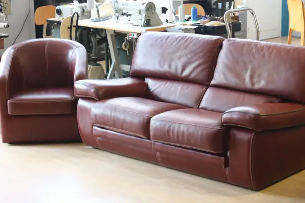 Un fauteuil et un canapé en cuir marron, avec des coutures blanches contrastantes, sont présentés dans un atelier.